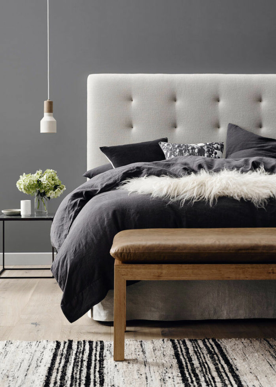 Foto: Barnaby Lane via Adore Säng med mörka textiler, grå sänggavel och en bänk framför