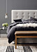 Säng med mörka textiler, grå sänggavel och en bänk framför