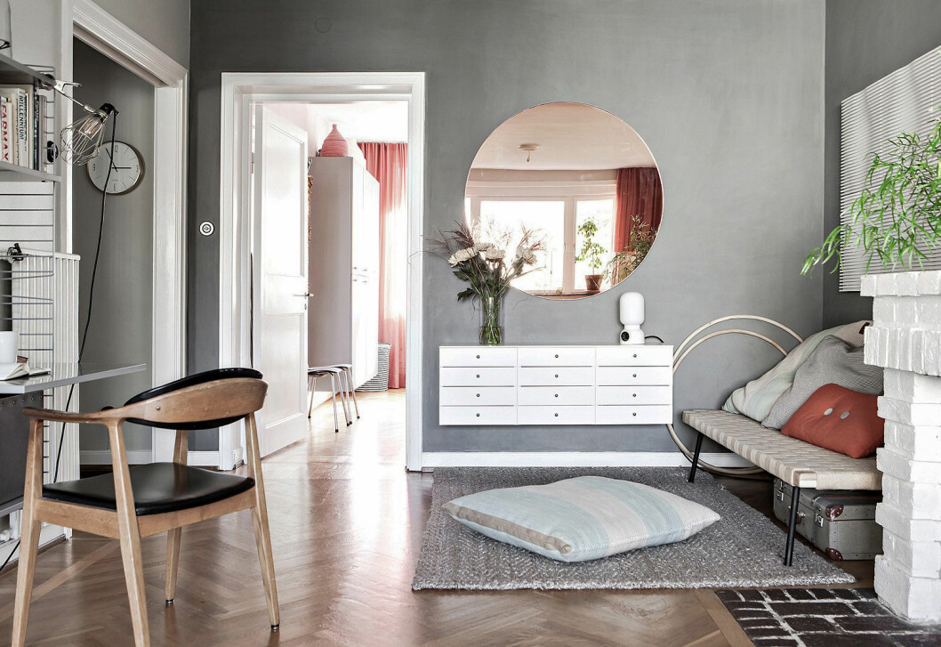 Gråmålad vägg i vardagsrum. Rund tonad spegel, dagbädd från Ikea och hyllsystem från String. 