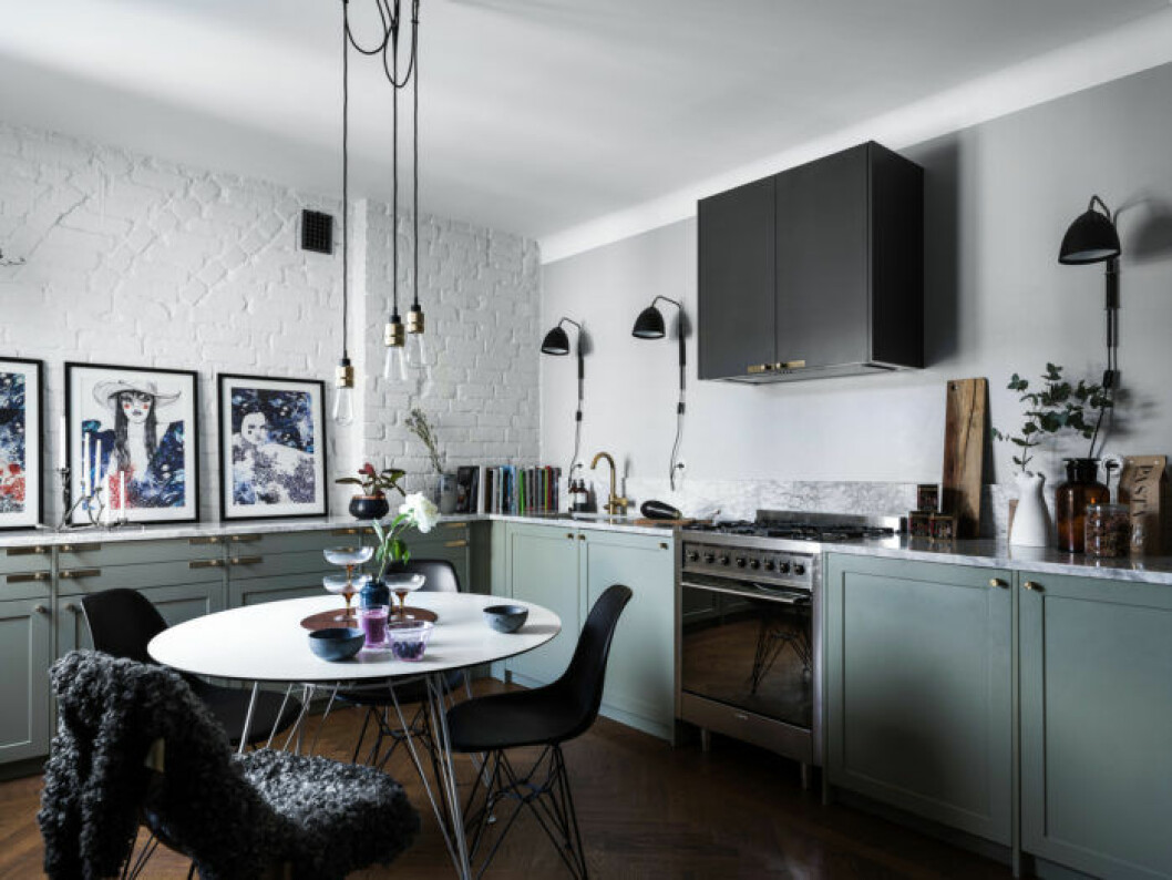 Grönt kök med en bevarad, vitmålad tegelvägg och stilren belysning