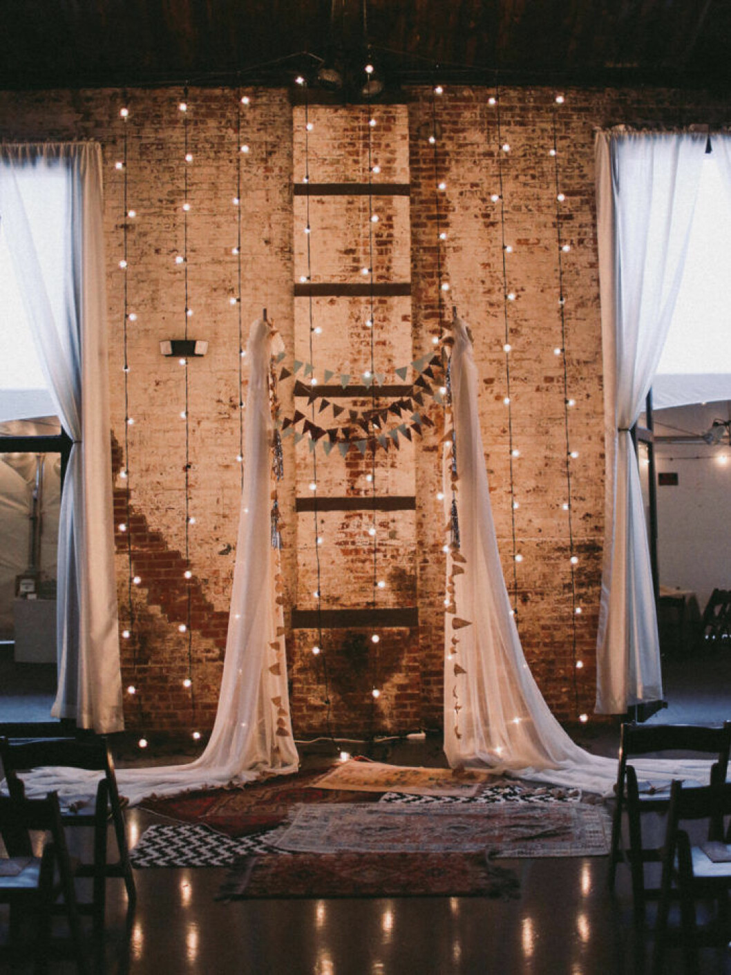 Backdrop med ljusslingor i en bröllopslokal med tegelvägg och högt tak.