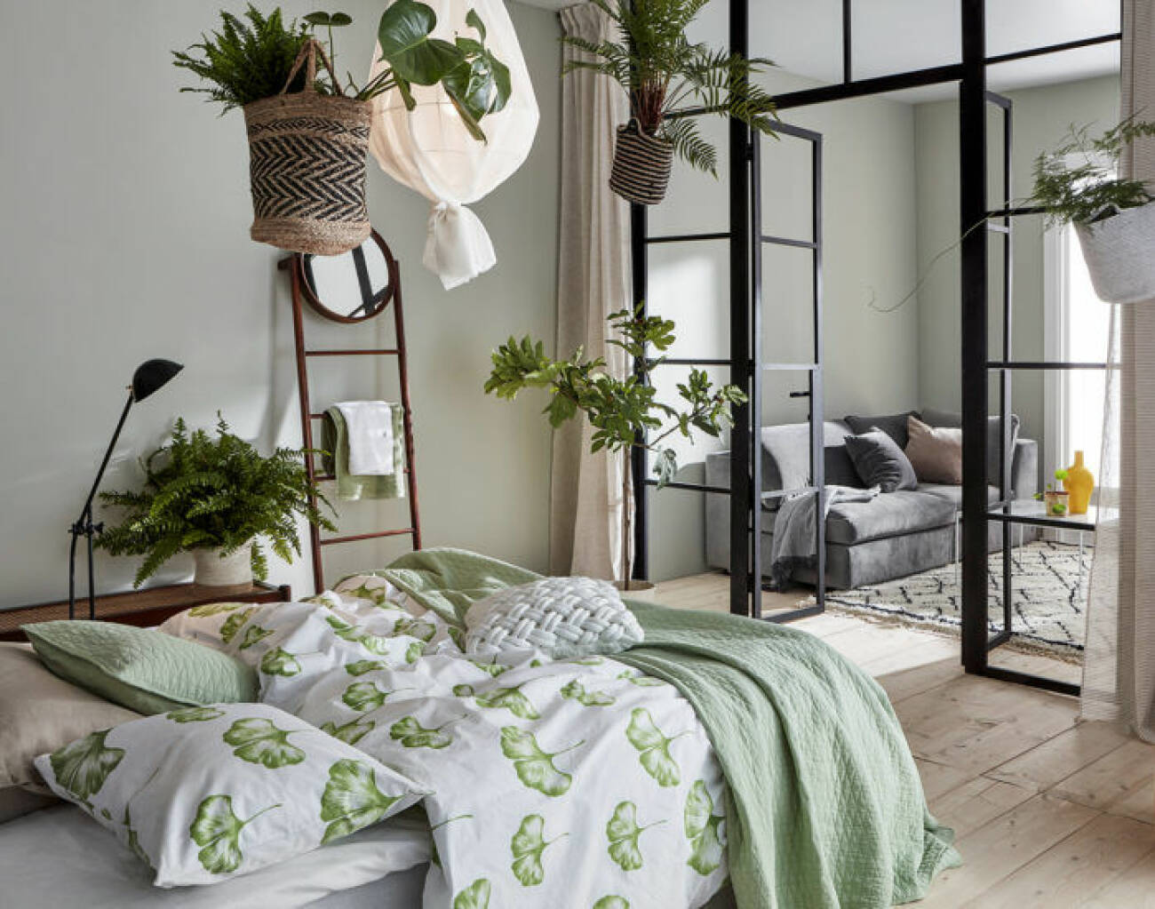 Sovrum med grönmönstrade sängkläder, växter i taket och glasvägg.