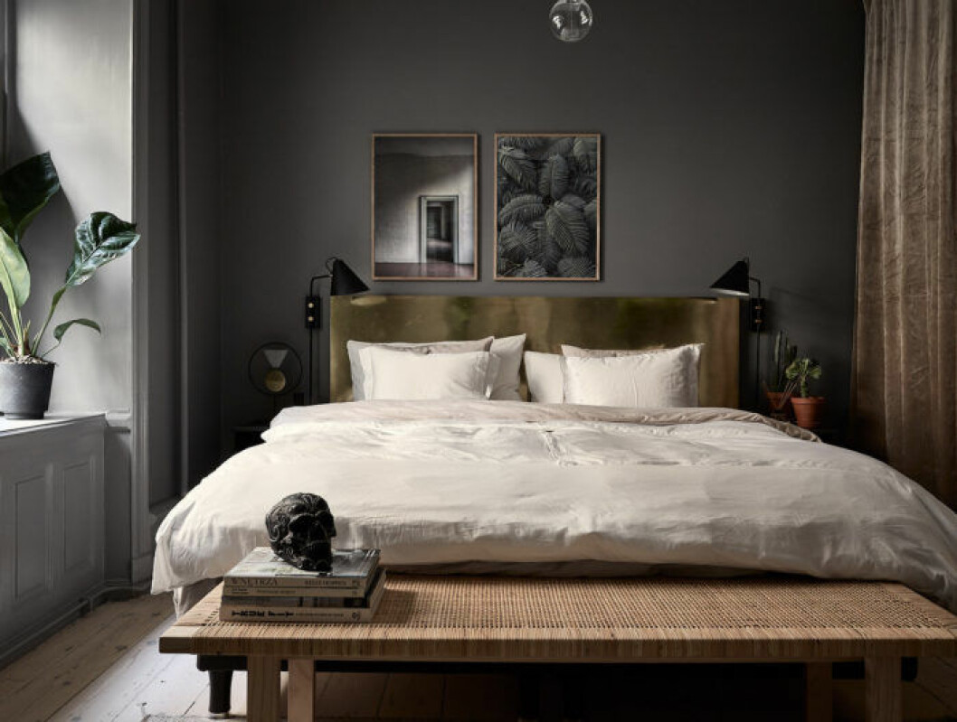 Sovrum med målade mörkgrå väggar, färg Mole's breath från Farrow & Ball. Sänggavel i mässing, tavlor ovanför sängen och rottingbänk från Ikea Stockholm 2017.