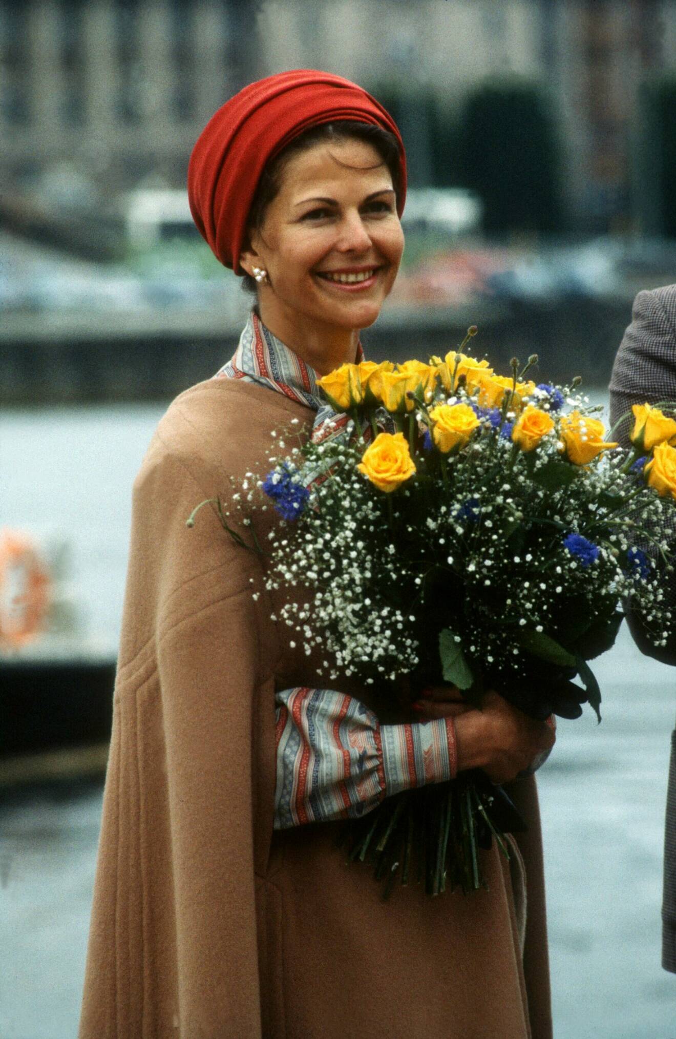 Drottning Silvia i en röd hatt och beige cape.