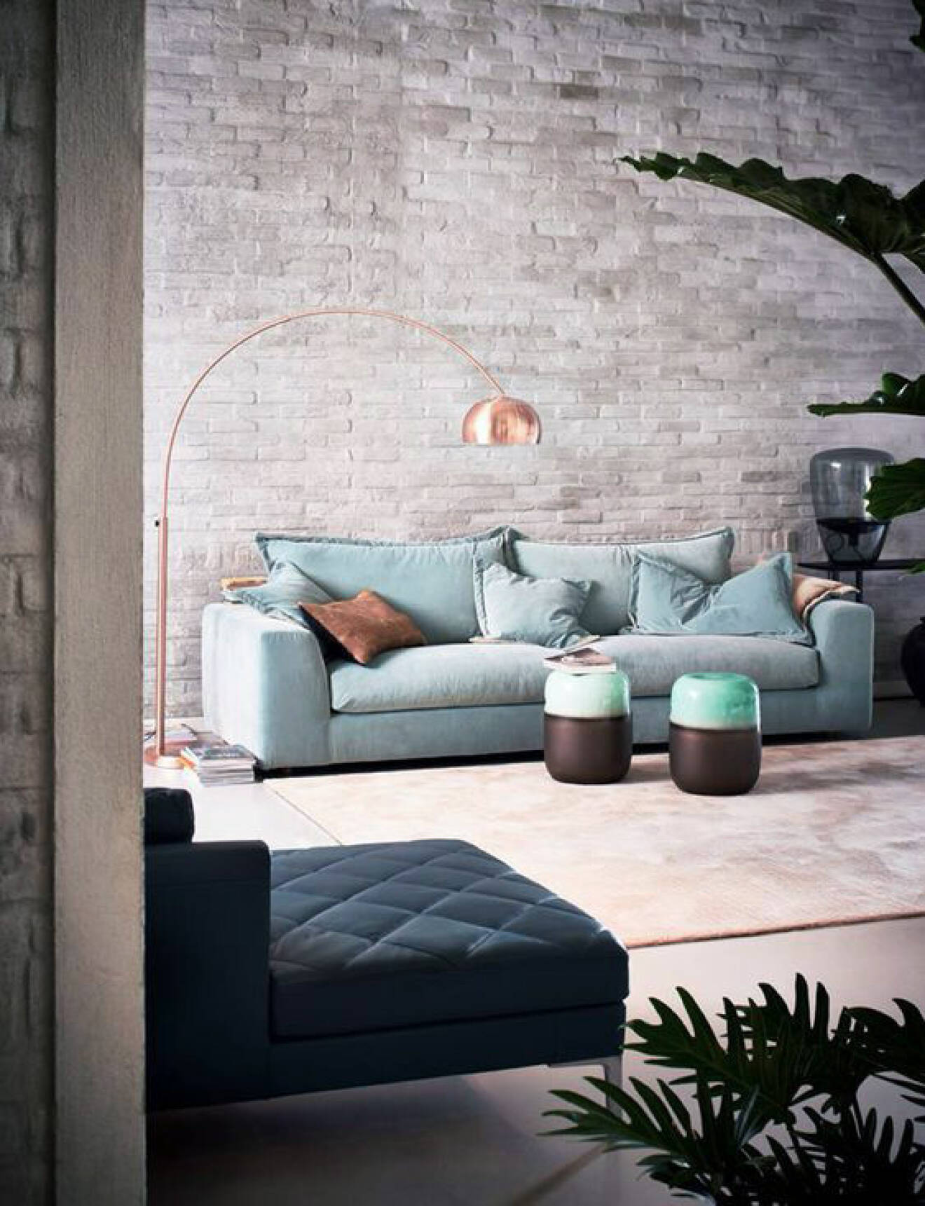 Tegelvägg mjukas upp av pastellblå soffa och mjuk sammet