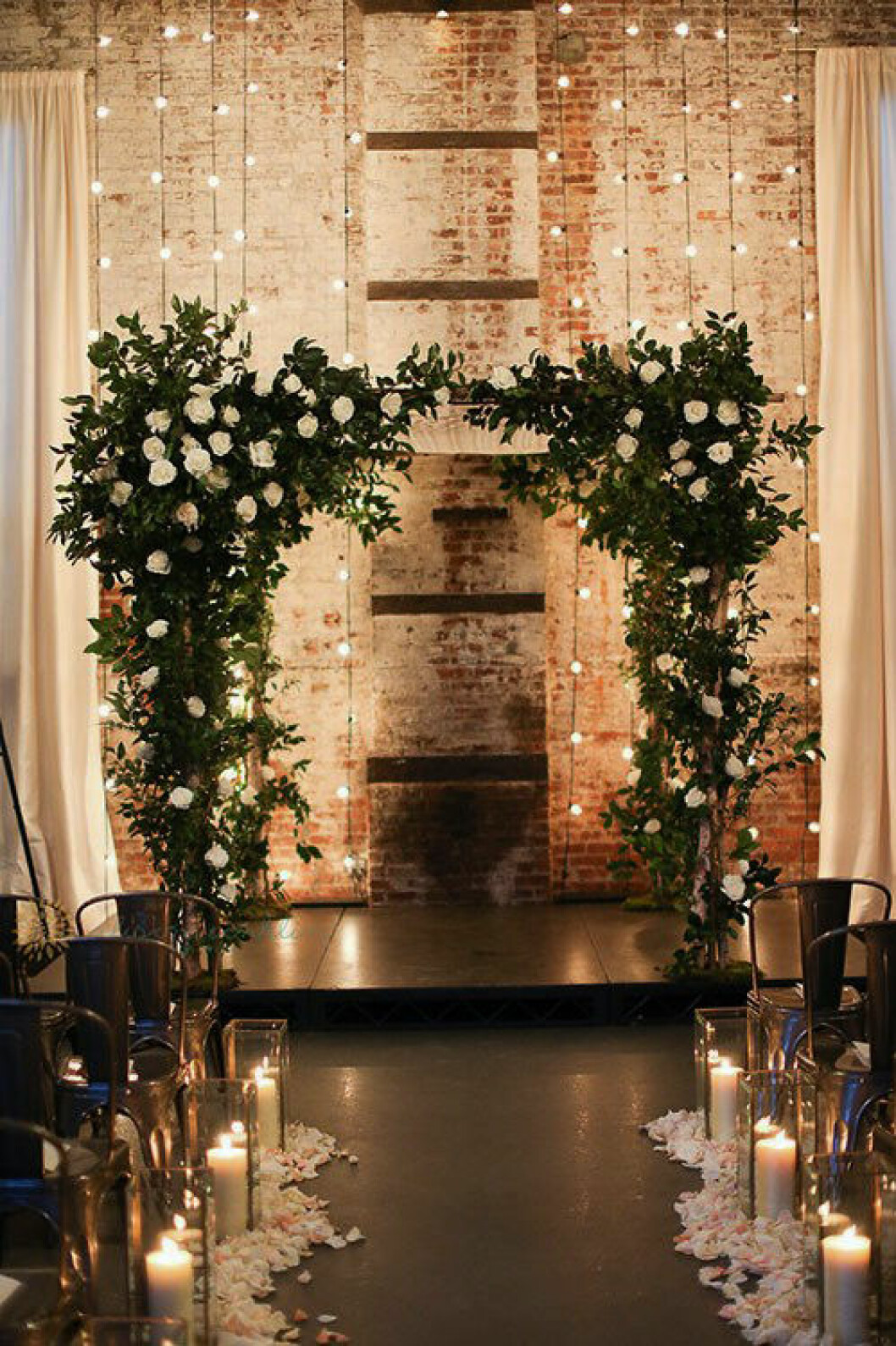 Foto: Alison Conklin photography via <a href="https://www.brides.com/story/brooklyn-wedding-ideas-the-green-building-alison-conklin-photography" target="_blank" rel="noopener">Brides</a> Backdrop med växter och ljusslingor. Bröllopslokal med högt i tak och tegelvägg.