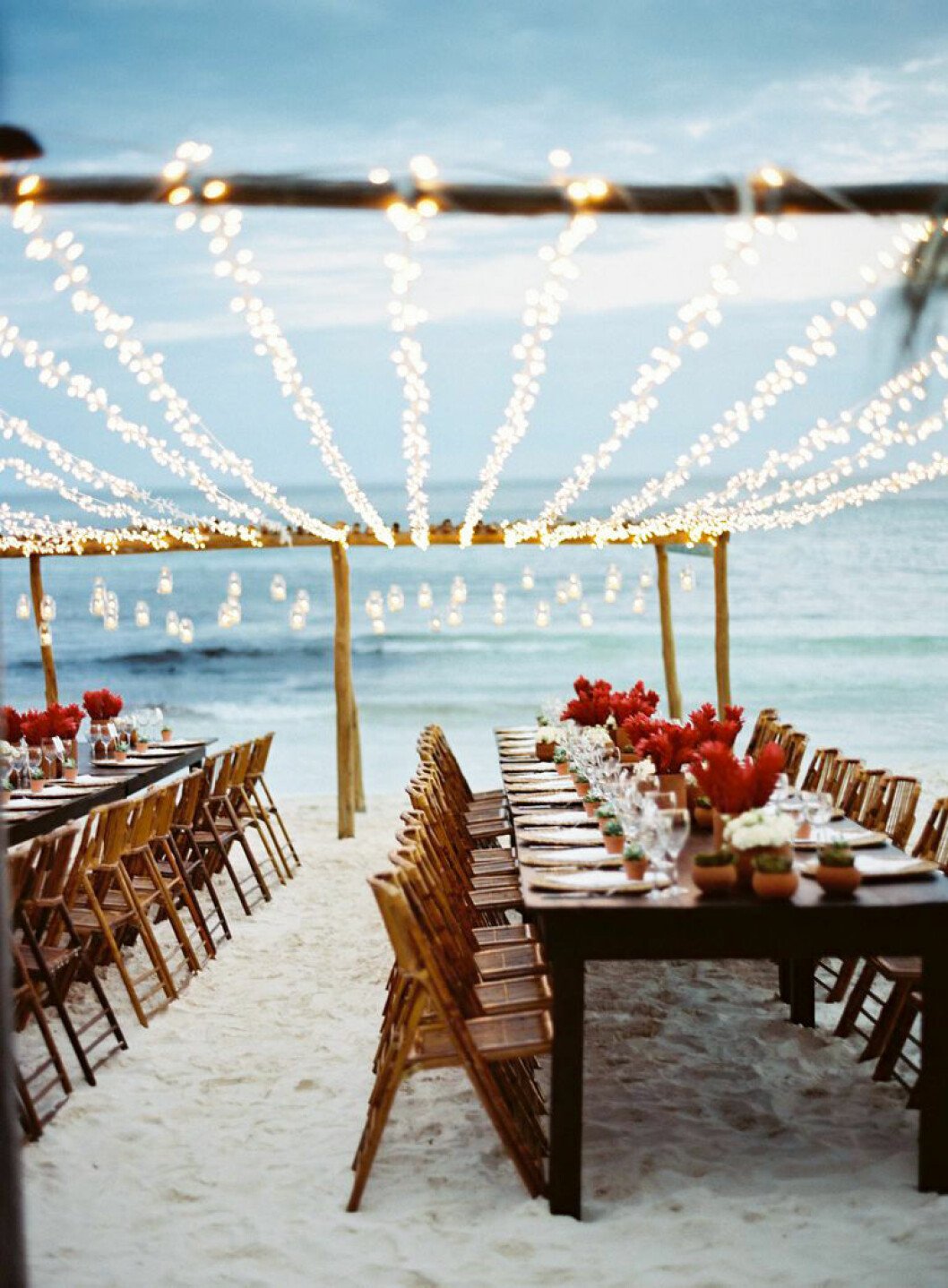 Strandbröllop vid havet, ljus sand och ljusslingor.
