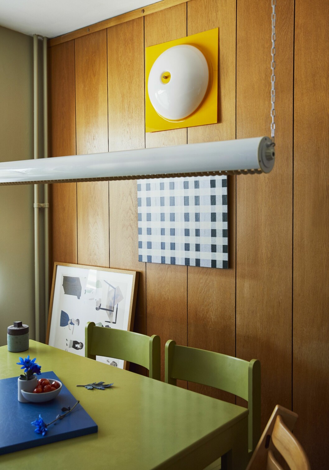 Panelen är kvar sedan en renovering på 70-talet. Konst av Jockum Nordström och Evelina Kroon. På väggen en plafond. Taklampa <span class=" italic" data-lab-italic_desktop="italic">Super tube</span>, design Anders Pehrson, Ateljé Lyktan. Bord och stolar, Stockholms auktionsverk. Liten skål av Shane Schneck. Evelina beskriver sig och sambon Gustaf From som en kombination av funktion och hopplös oreda. ”När vi egentligen behöver fixa en hallförvaring börjar jag sätta upp tavlor.” konst och inredningsdetaljer hos evelina kroon