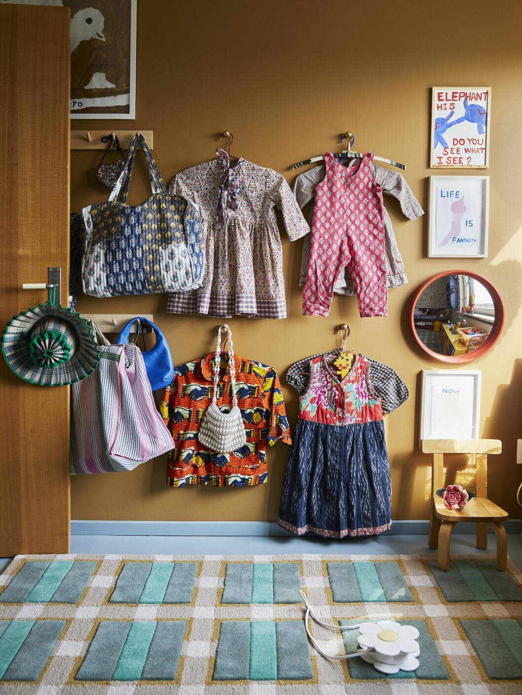 Posters i barnrummet av bland andra Mogu Takahashi/Fine little day och David Shrigley. Övre raden: Klänning och byxdress, STREJK. Undre raden: Skjorta, Mixed grill banjul. Spegel <em>Konvex</em>, design Josef Frank, Svenskt tenn. Knopplist, Iris Hantverk. Väggknoppar i mässing, Byggfabriken. barnens rum hos evelina kroon