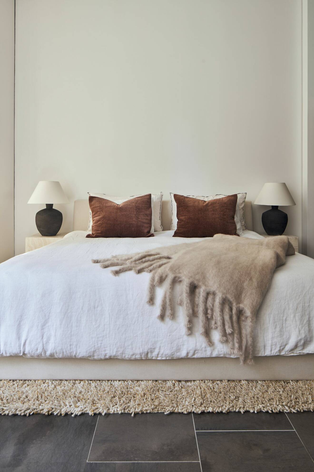 Minimalistiskt sovrum med bruna kuddar och varma toner