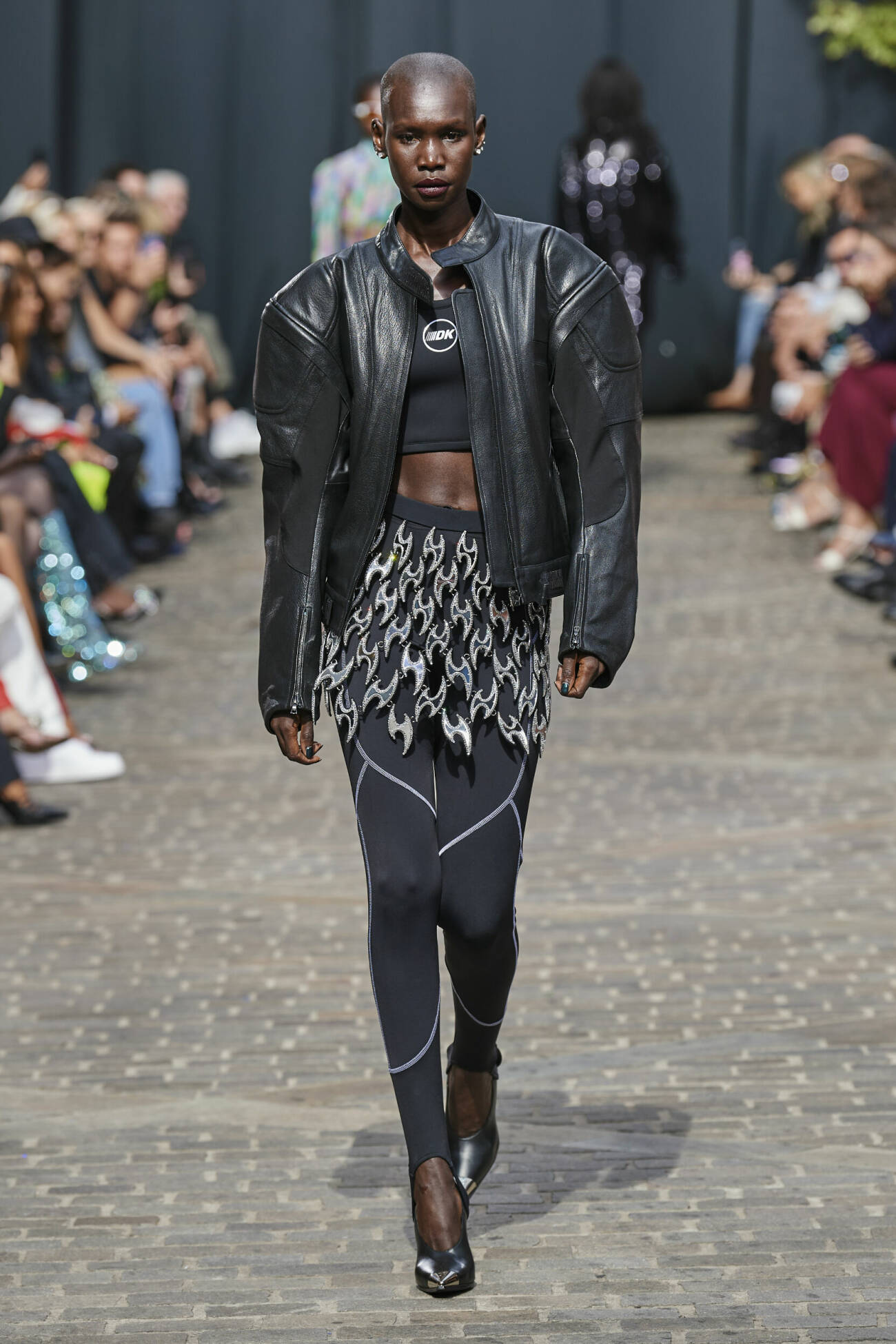 Modell i svart bikerjacka med svart magtröja, leggings och kjol med silvriga detaljer, David Koma SS23
