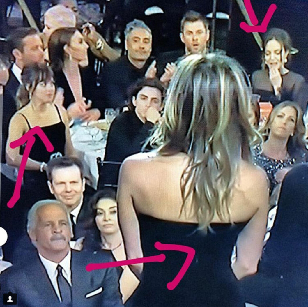 Dakota Johnson tittar på Angelina Jolie som ignorerar Jennifer Aniston uppe på scenen.