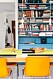 En platsbyggd bokhylla är målad i en mättad turkos färg som minner om gamla industrier från 50-talet. Bordets vaxduk, lampornas sladdar och loppisstolarna i gult utgör en pigg kontrast. Mässingsljusstakarna kommer från en loppis och skålen är av Tom Dixon.