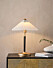 miljöbild på bordslampa med svart och guldig fot och vit plisserad lampskärm från jotex
