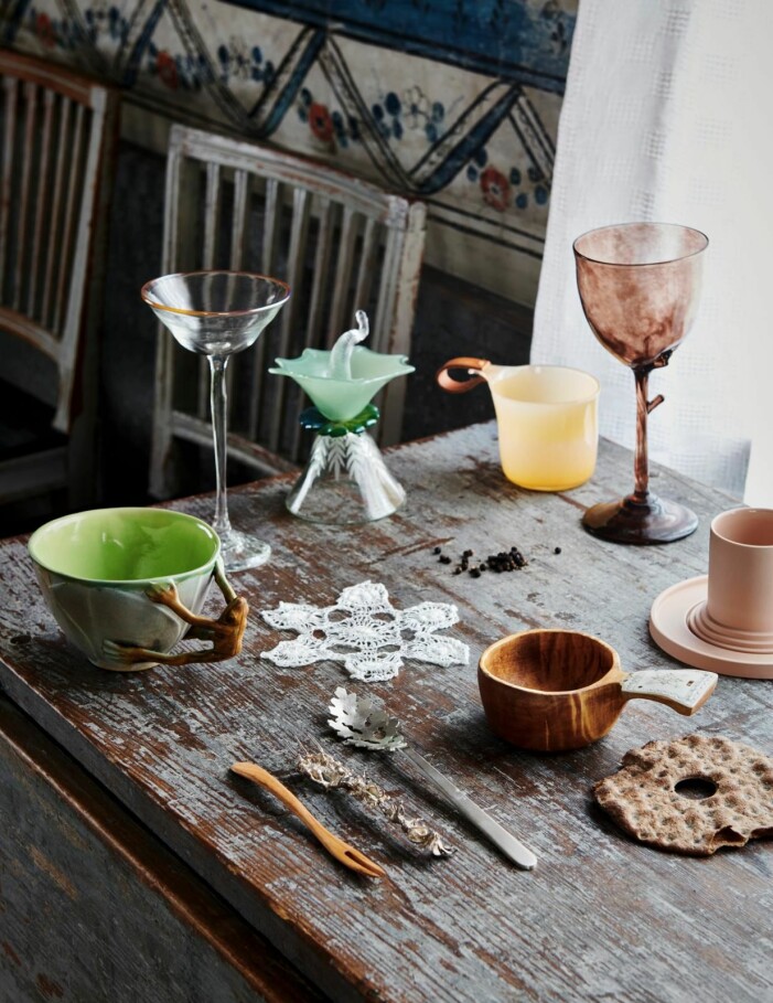 Nilla Eneroth har tolkat den traditionella kåsan i persikofärgat glas, 400 kr, Blås & Knåda. Bruna vinglaset <span class=" italic" data-lab-italic_desktop="italic">Skog </span>av Ulla Gustafsson, 980 kr, Blås & Knåda. Intill skymtar kopp och fat Amal, 615 kr, Sizar Alexis. En traditionell kåsa av trä och renhorn av Johan Farkk, 7 500 kr, Svensk Hemslöjd. Silversked av Katarina Henriksson, 15 000 kr/2 st, och gaffel av Åsa Elmstam, 7 500 kr, båda Konsthantverkarna. Trägaffel, 39 kr, samt liten virkad duk i form av en snöflinga, 39 kr, Skansenbutiken. Mugg med handtag i form av en groda, 650 kr, Jakob Danhard. Högt glas med orange kant, 990 kr, och blomformad dekoration i glas, 1 150 kr, båda av AnnaLena Rudolfsson, Blås & Knåda. Så inreder du med trendstilen cottagecore