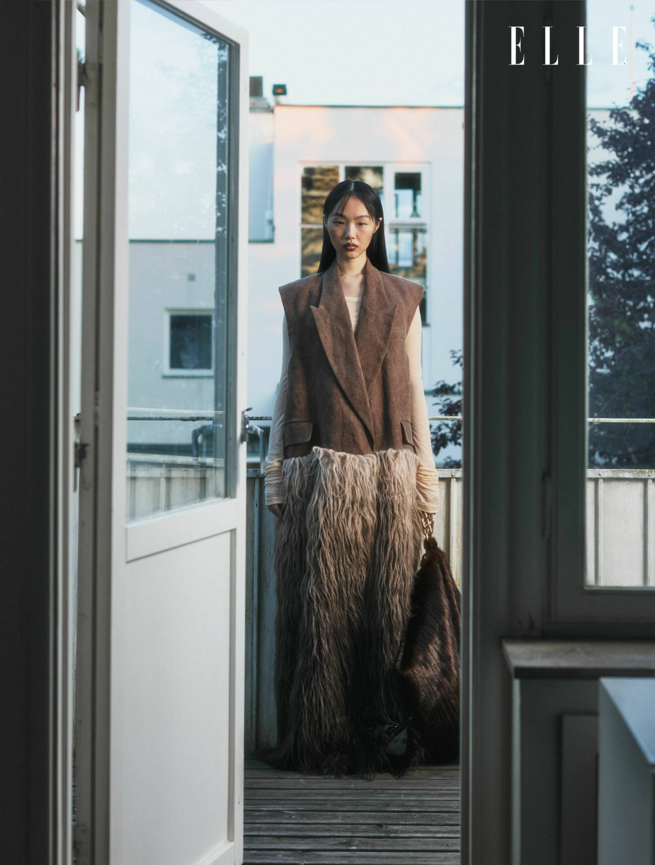Modellen står på en balkong, klädd i en väst med fuskpäls från Uma Wang