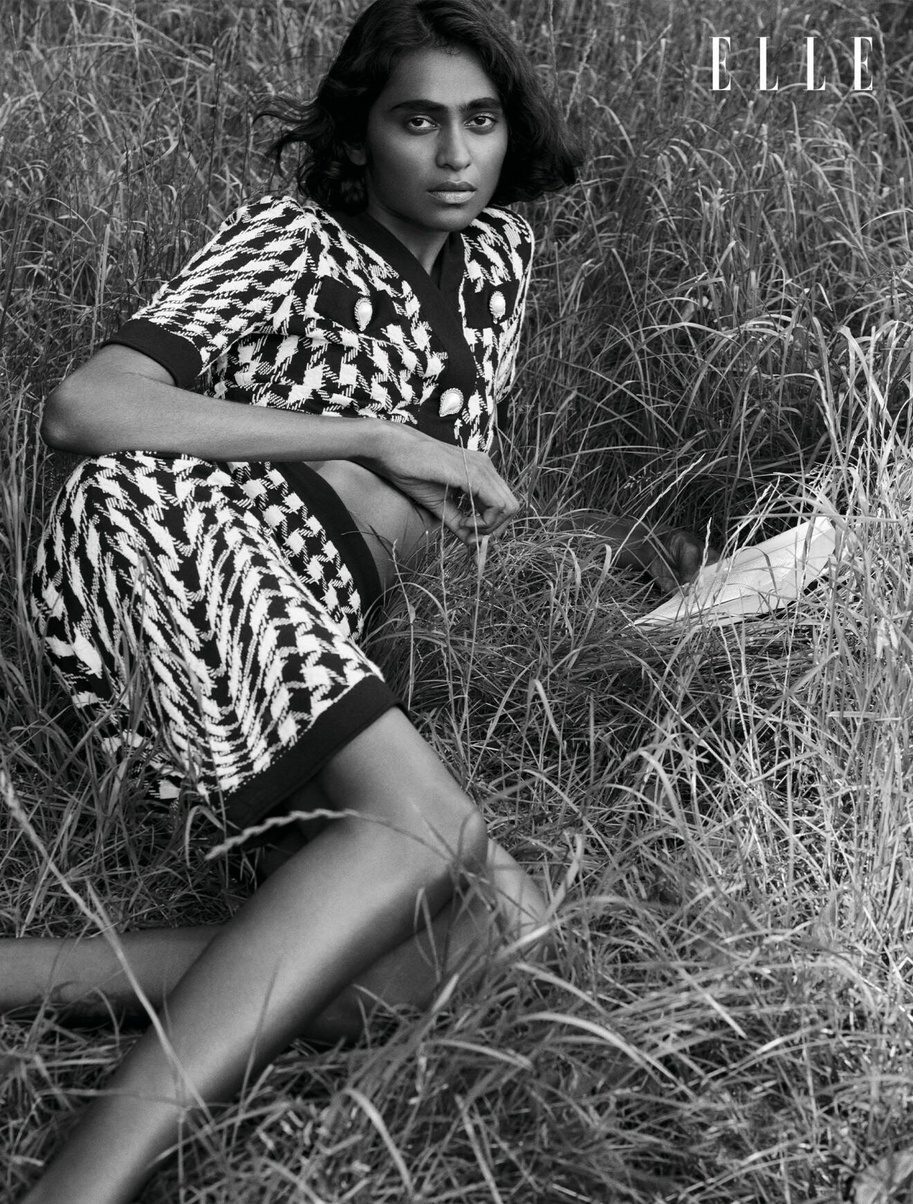 Modellen Barathy ligger i gräset, hon bär matchande topp och kjol i svartvitt mönster, från Moschino.