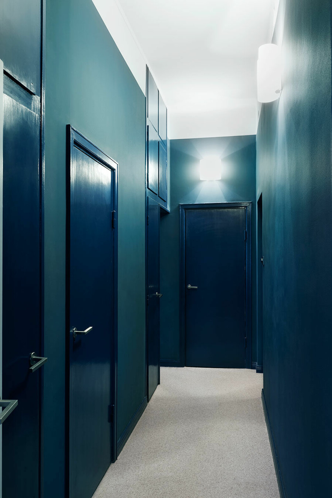 Korridoren med klädkammaren i ena änden och de tre sovrummen i fil längs med ytterväggen. Den avskilda privata känslan förstärks av den omboande heltäckningsmattan och färgvalen. Väggarna är målade i en helmatt blå nyans som står i effektfull kontrast mot dörrar och listers högblanka finish. ”Jag ville egentligen ha ännu mer färg”, säger Clara.