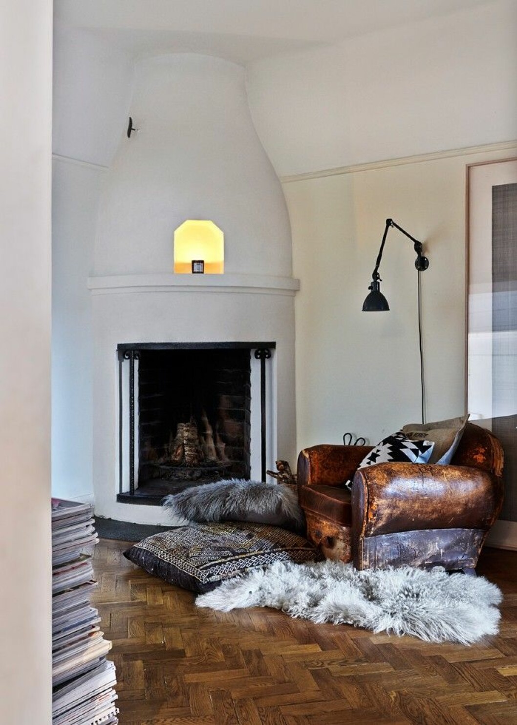 Framför den öppna spisen i inre hallen finns plats för vila. Fårskinn från Paris, vintagekudde i kelimväv. Mot väggen anas ett stort konstverk av Sophie Tottie. Platsen vid den öppna spisen är en plats för vila.