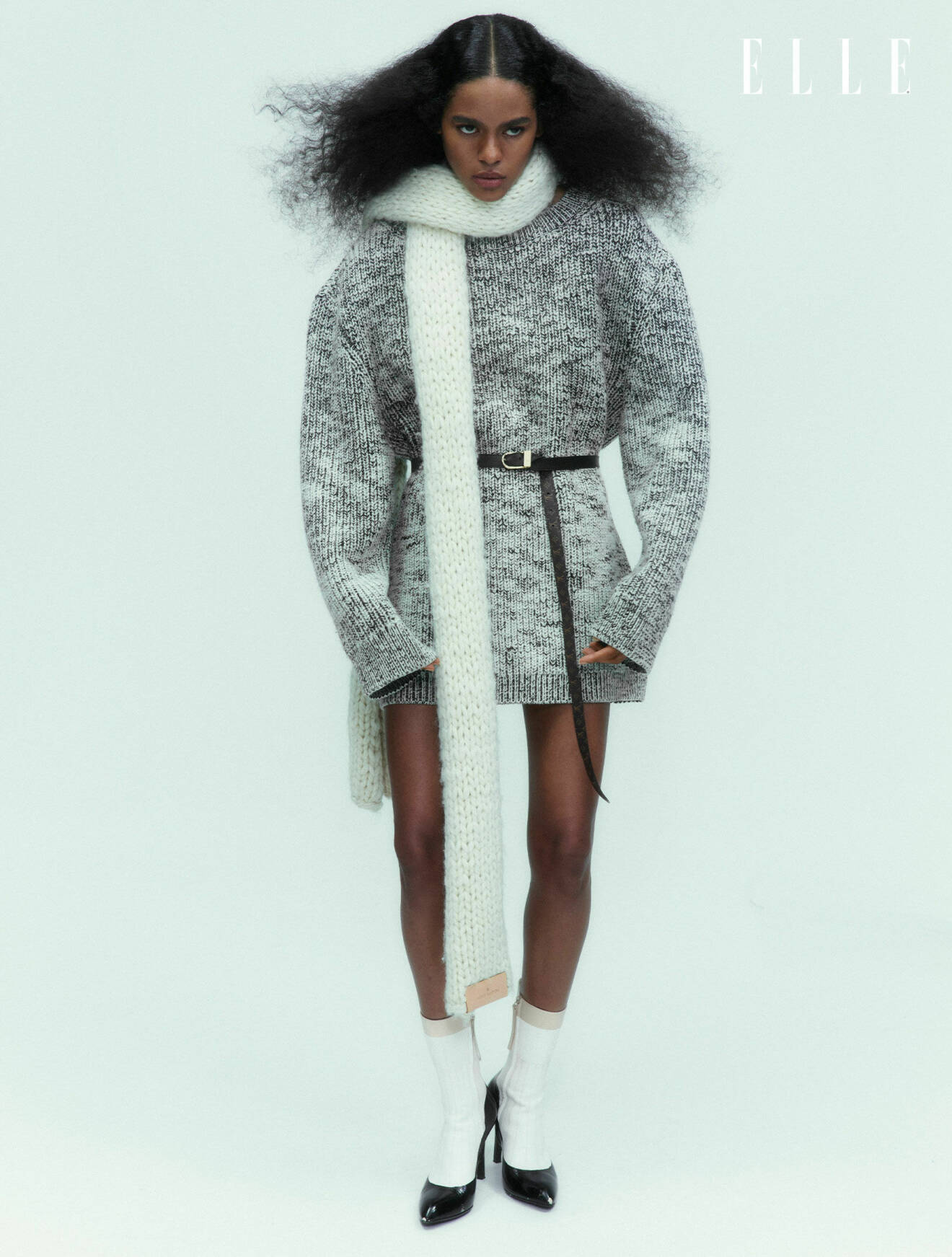 Fotomodellen bär en stickad klänning i grått och en vit stickad halsduk, allt från Louis Vuitton