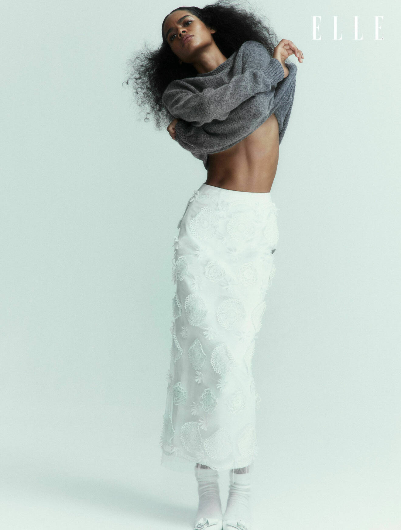 Modellen har på sig en grå stickad tröja och en lång vit kjol, båda från Prada