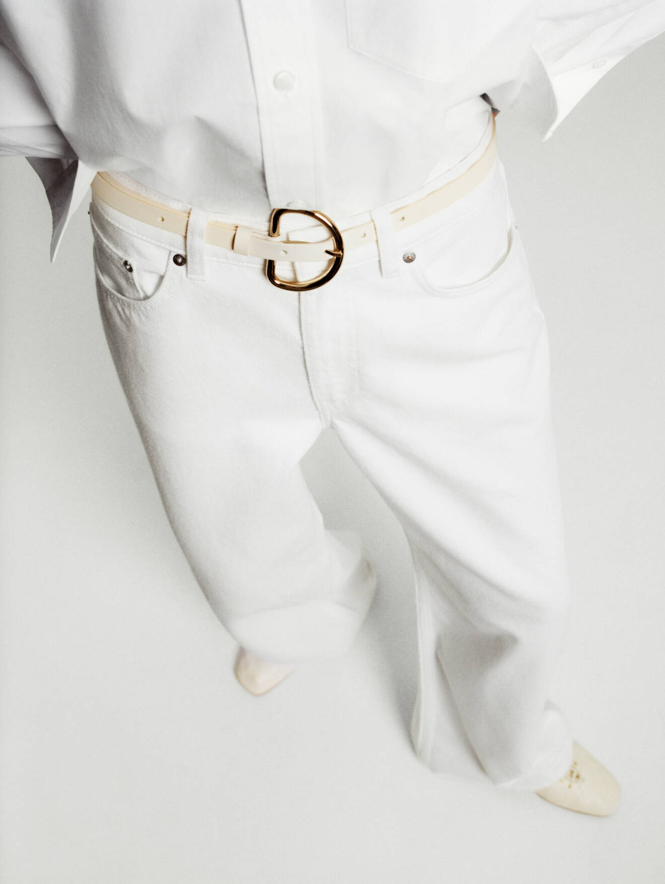 Vita jeans och ett krämvitt bälte med guldspänne.