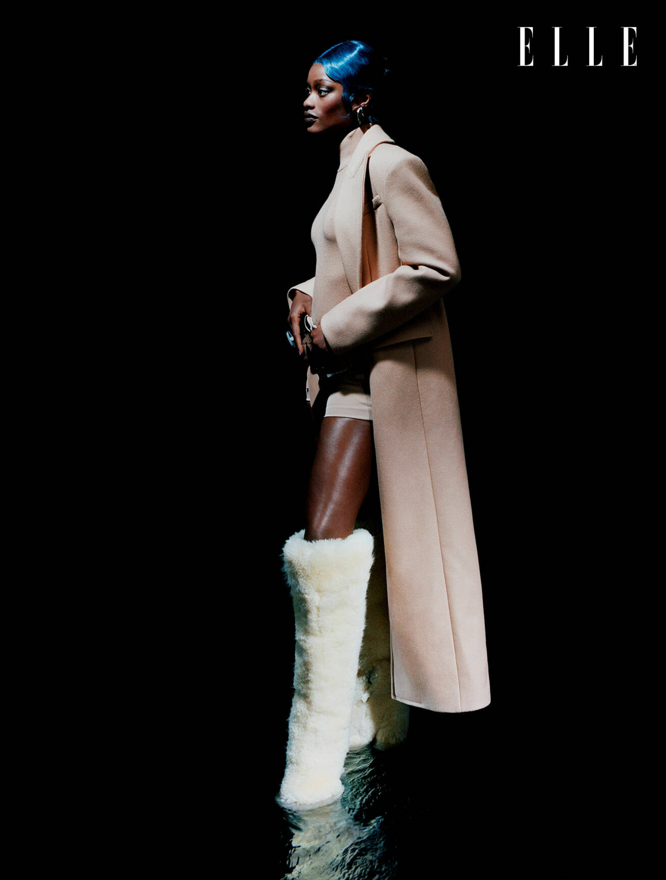 Modellen har på sig en beige lång jacka, shorts och bälte, allt från Michael Kors Collection, tillsammans med vita shearlingstövlar från Duran Lantink
