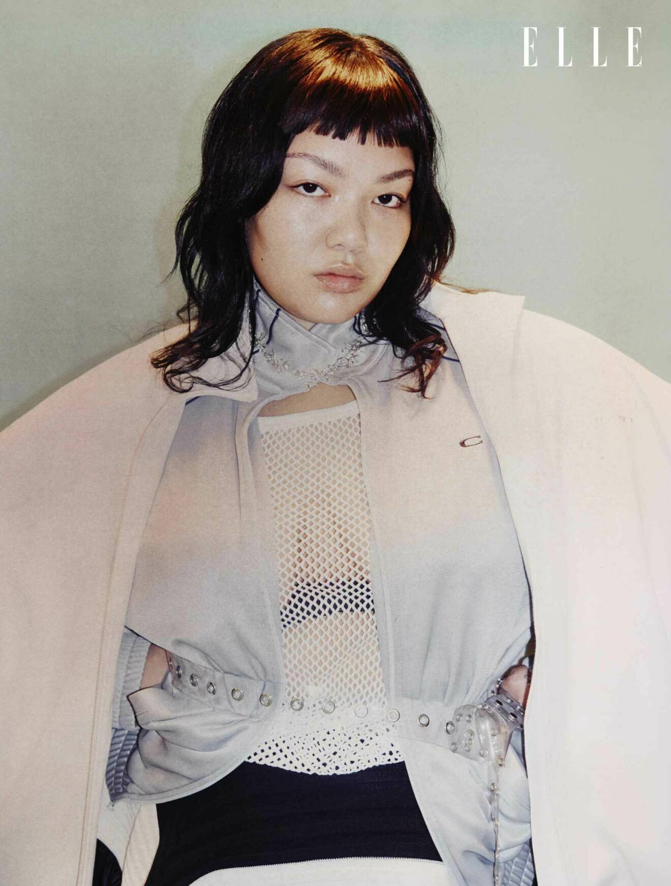 Fotomodellen bär en crèmevit tracksuitjacka, från Isabel Marant, med en grå tracksuitjacka under, från Commision, med ett vitt nätlinne, från Resteröds