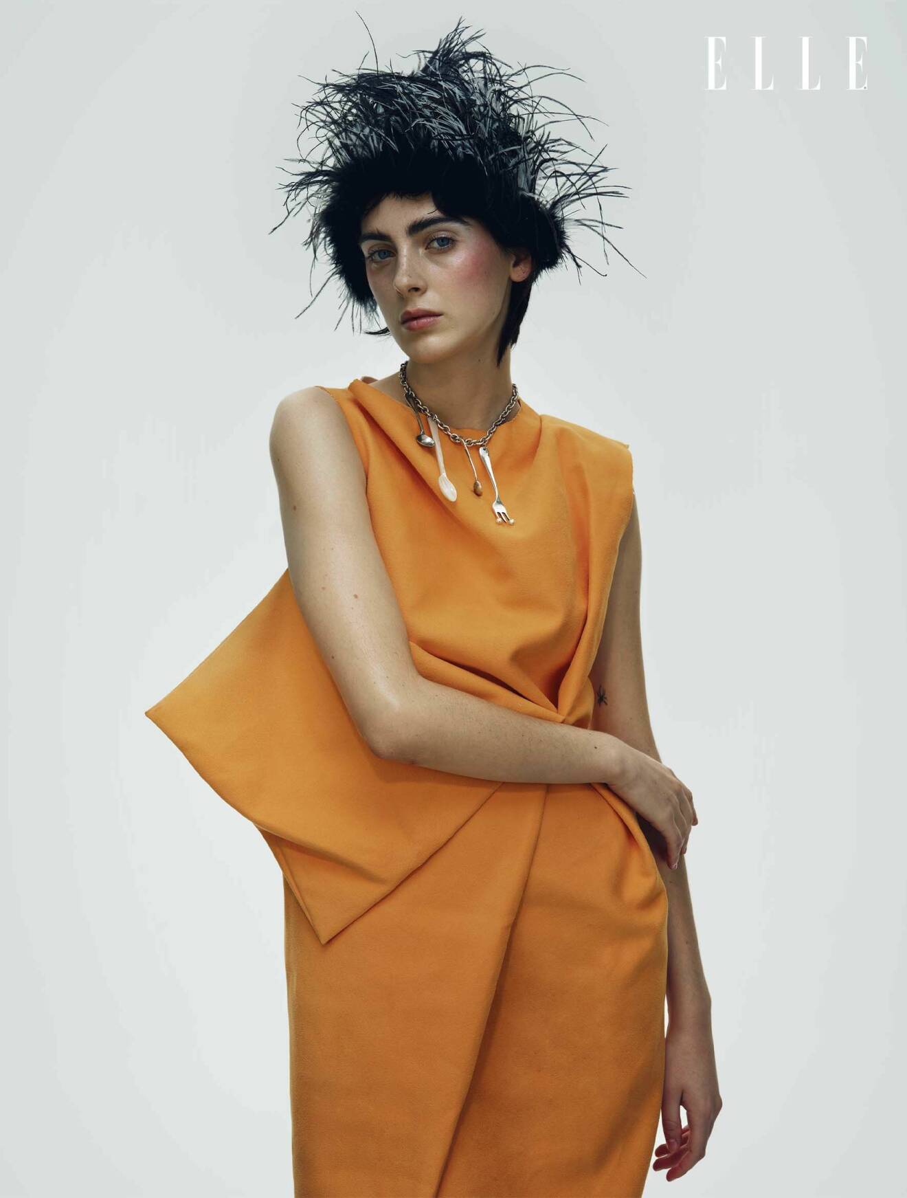 Modellen har på sig en orange klänning från Etre och en fjäderhatt från Nicklas Skovgaard