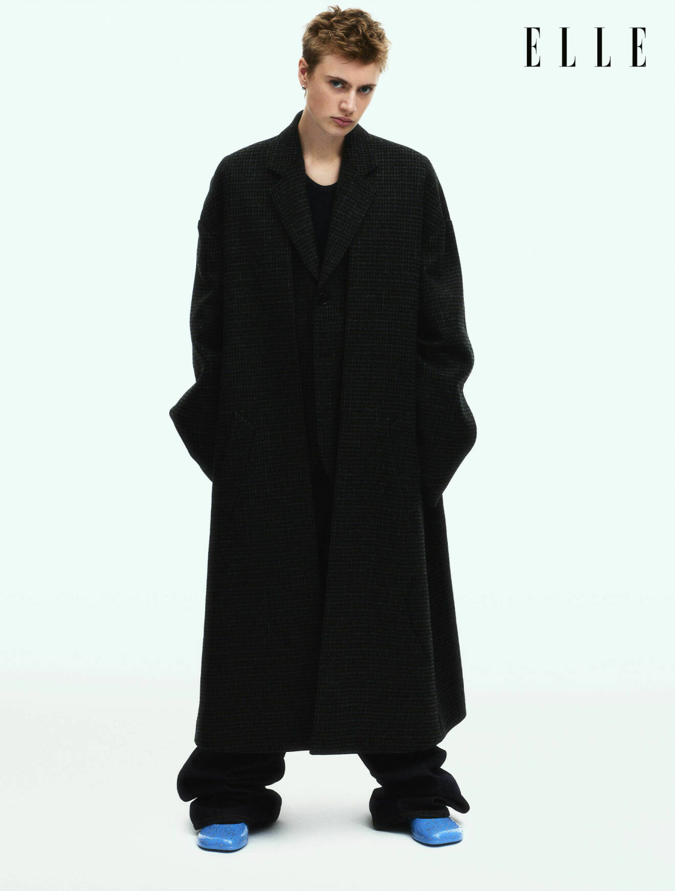 Modellen Elio Berenett är klädd i svart kappa, jeans och blåa skor, allt från Loewe.
