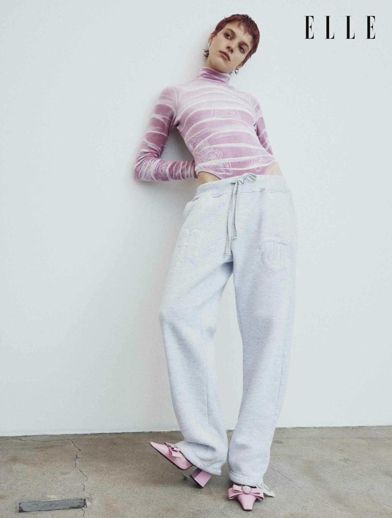 Modellen lutar sig på en vägg, hon har på sig en rosa body och ljusa mjukisbyxor