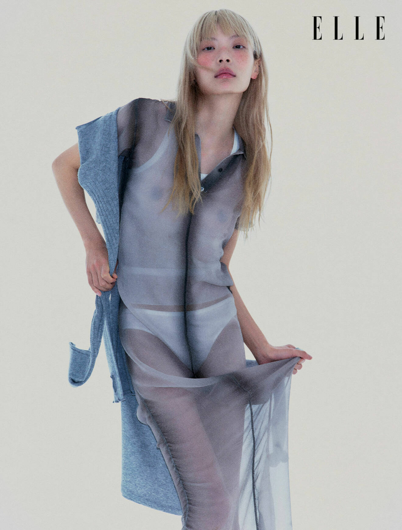 Modellen har på sig en lång genomskinlig klänning från Loewe med en stickad tröja från Filippa K.
