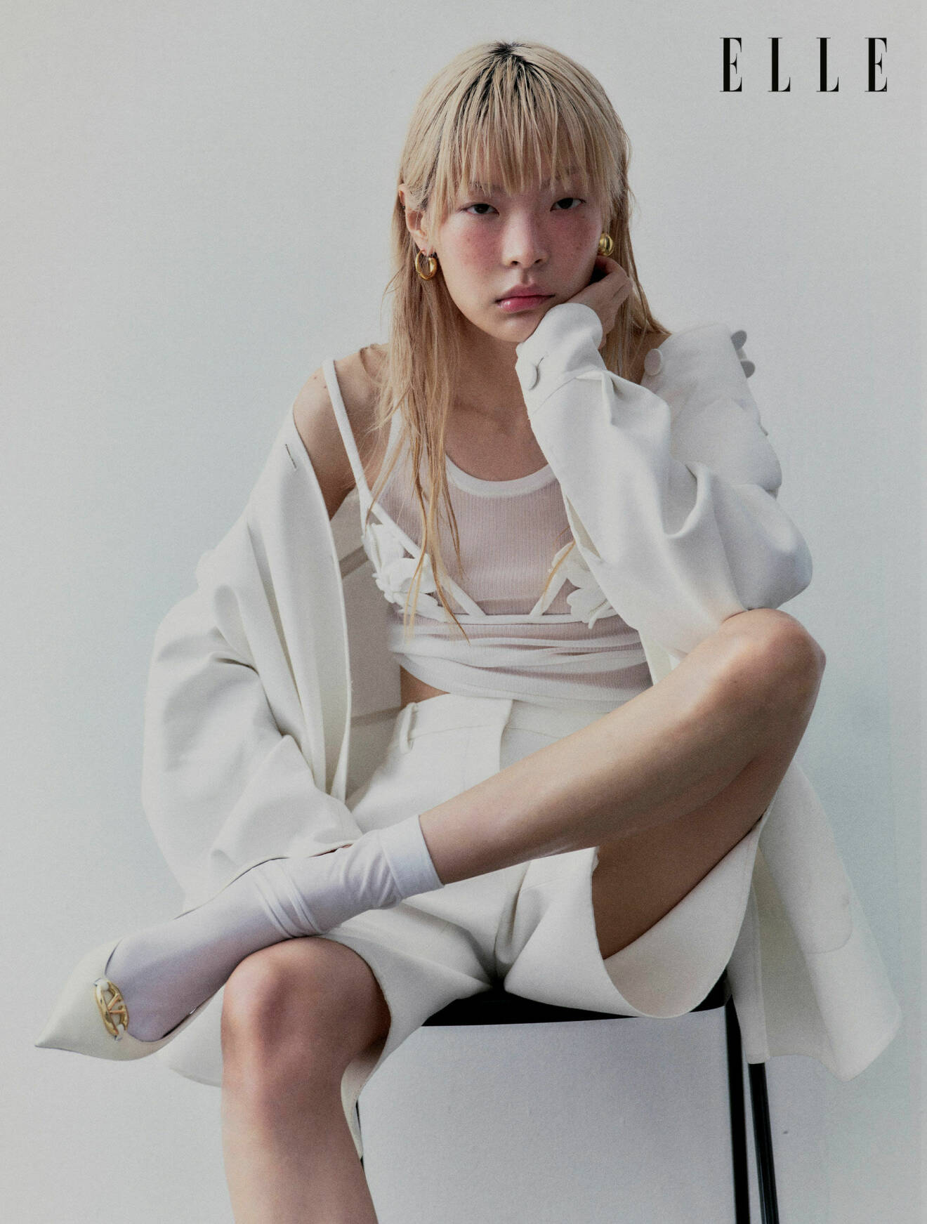 Modellen sitter ner, hon har på sig en vit skjorta, topp shorts och skor, allt från Valentino