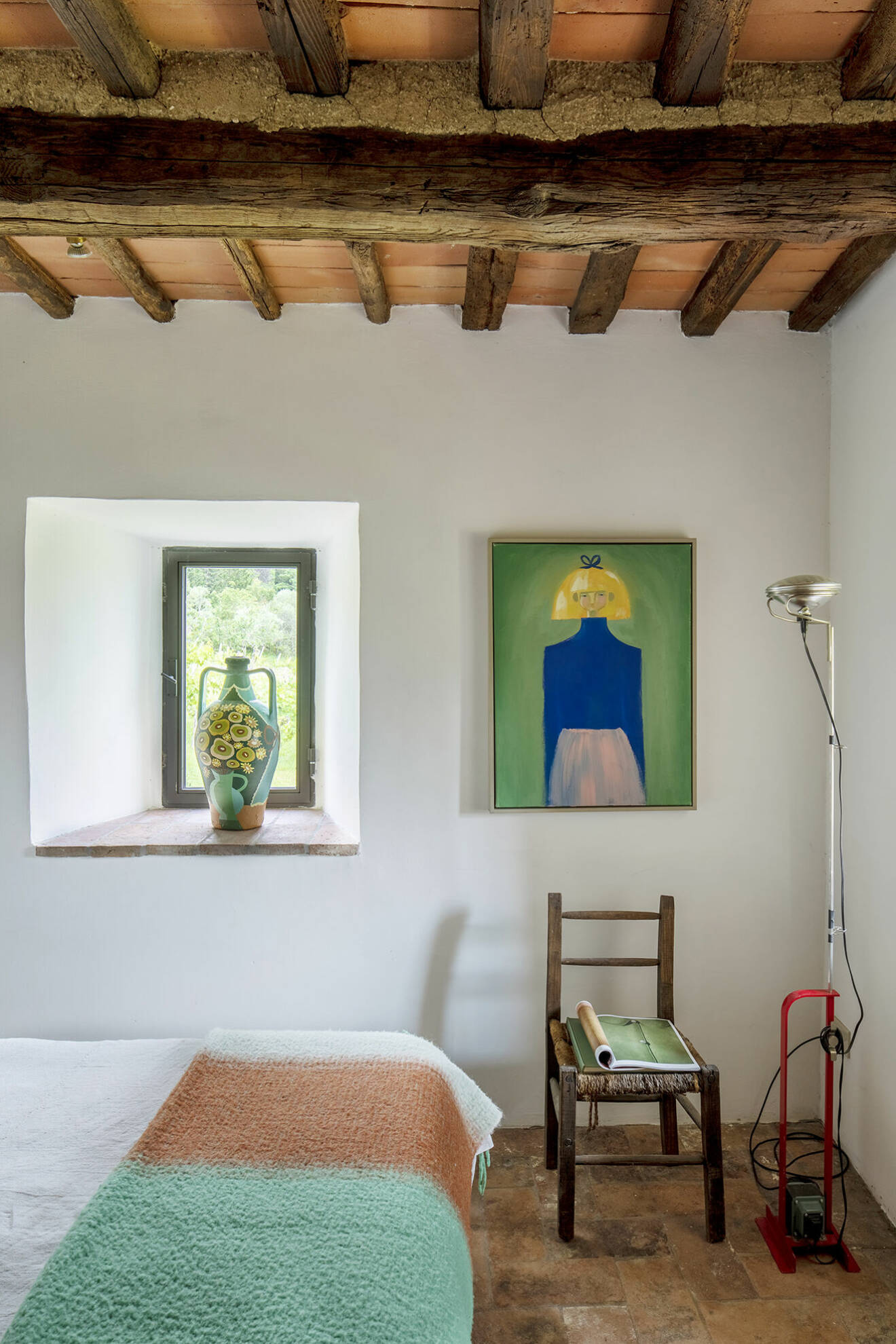 Minimalistiskt sovrum med fönsterglugg mot grönskan. Överkast, Rodebjer. Lampa Toio, Flos. All konst av Liselotte.