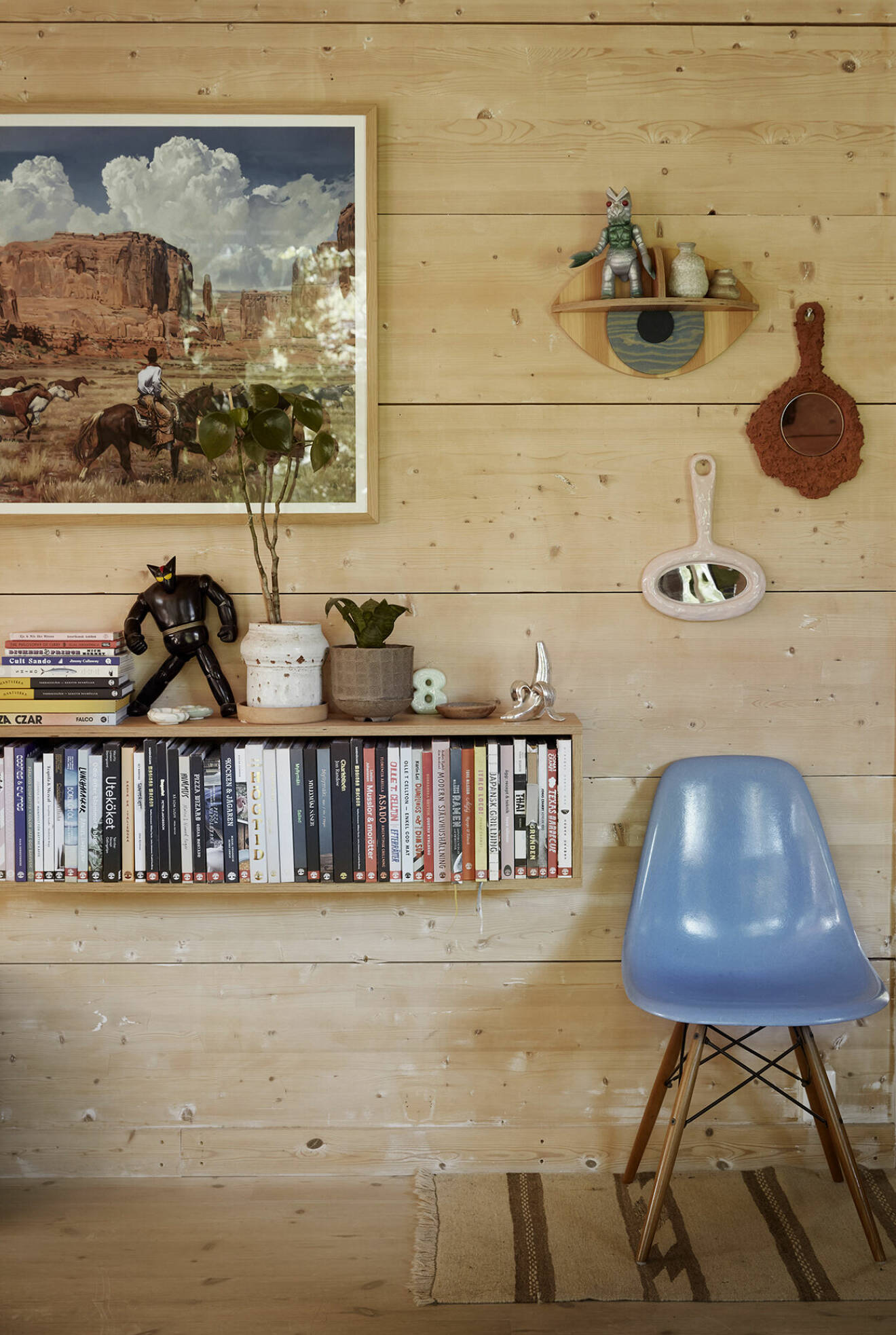 Böcker, reseminne, konstobjekt och tavlor. Fin backdrop med de trärena balkarna. Eames Plastic side chair för Vitra.Tavlan från amerikanska västern är gjord av Mark Maggiori, en franskamerikansk målare.