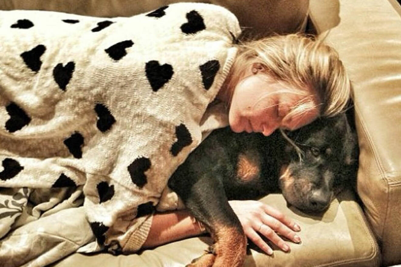 En kvinna ligger i en soffa och myser med sin hund.