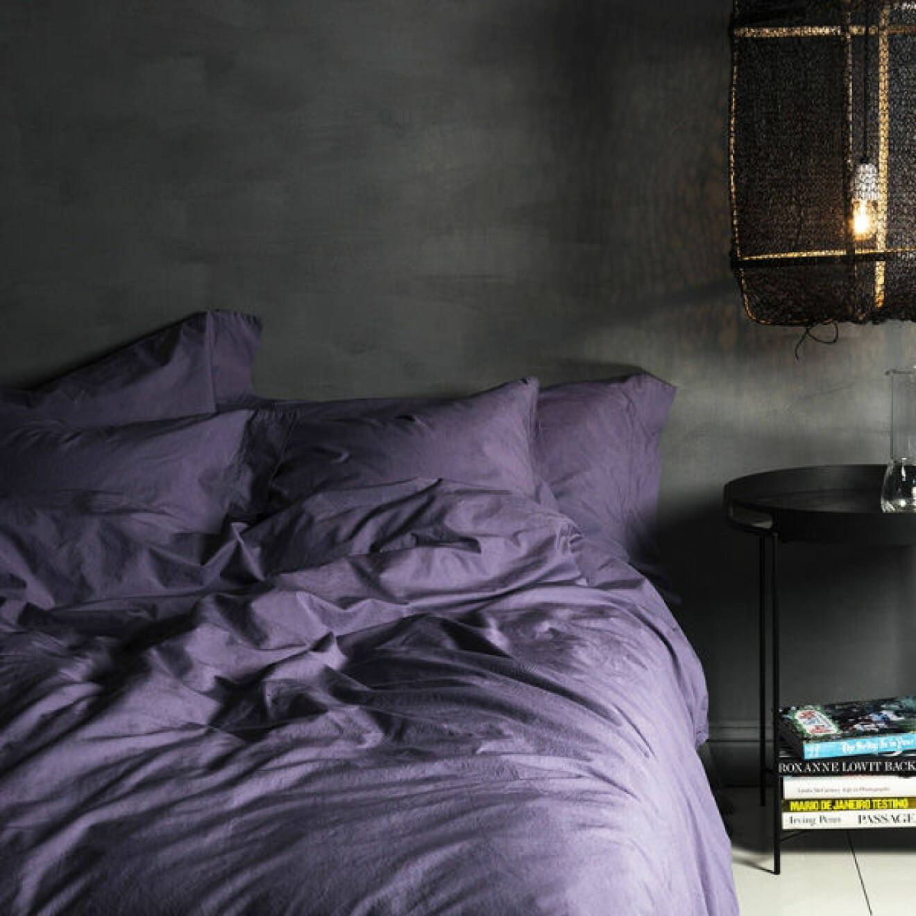 Mörk sovrum med säng bäddad med violfärgade lakan.