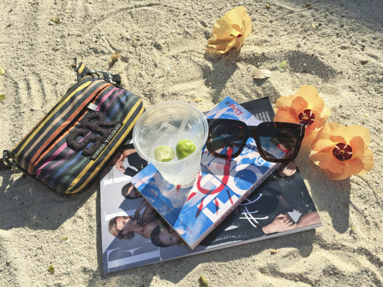 ELLE-magasin, bok, solglasögon och blommor på en strand.