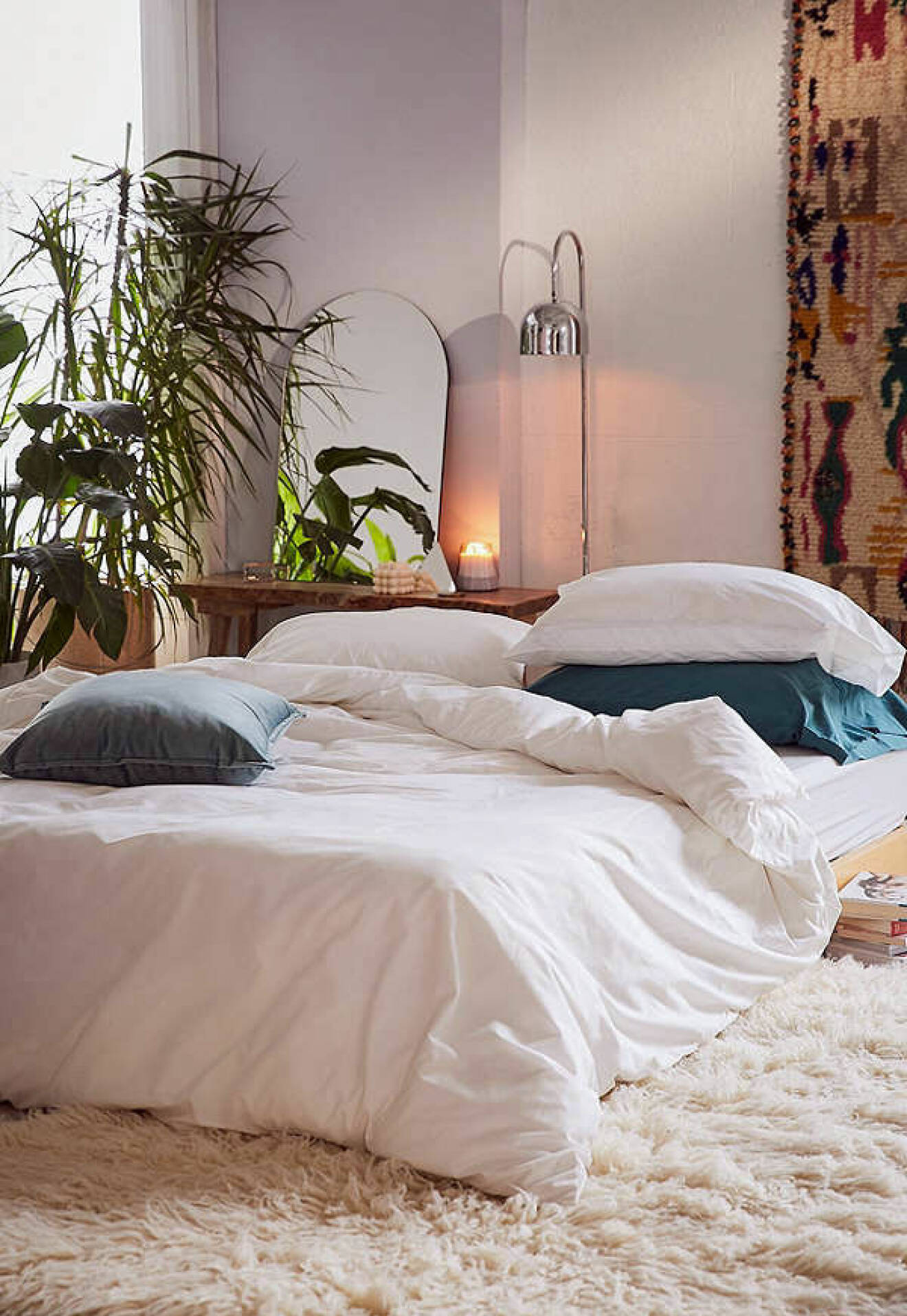 Vit säng i ombonad omgivning med växter och textilier