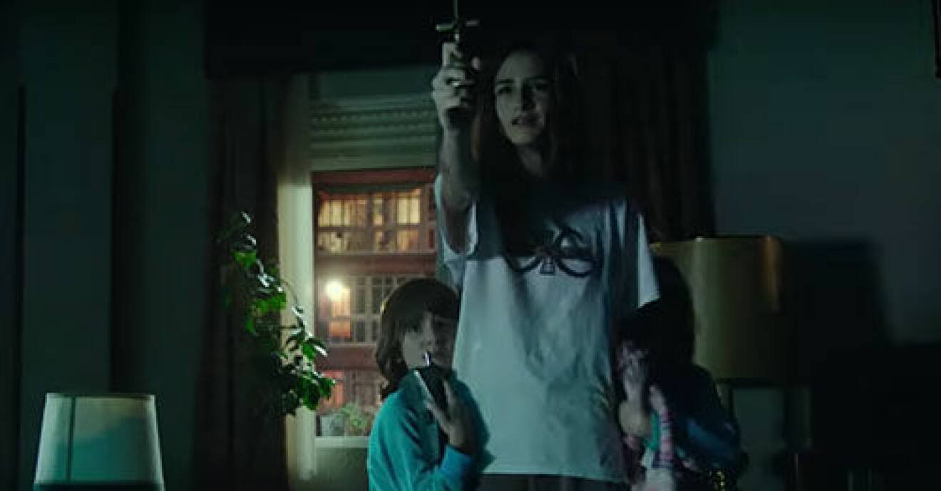 Veronica håller upp ett kors för att skydda sig själv och sin lillebror mot onda andar i skräckfilmen Veronica som finns på Netflix.