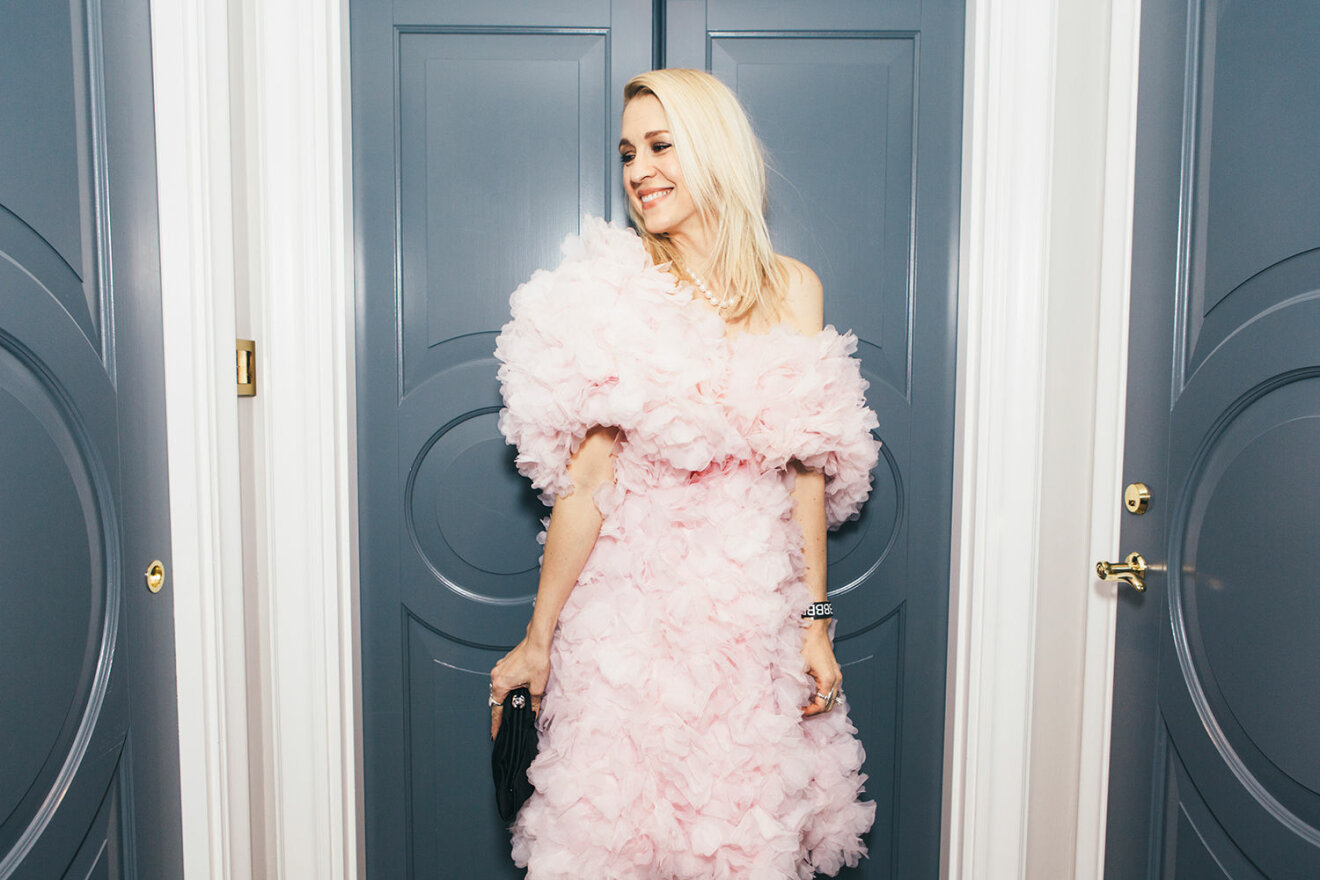 Emilia De Poret i fluffig rosa klänning vid blåa dörrar.