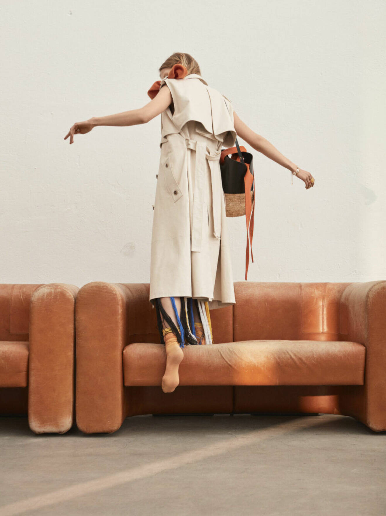 Modell står på rostbrun soffa i ljusbeige kappa från Bottega Veneta.
