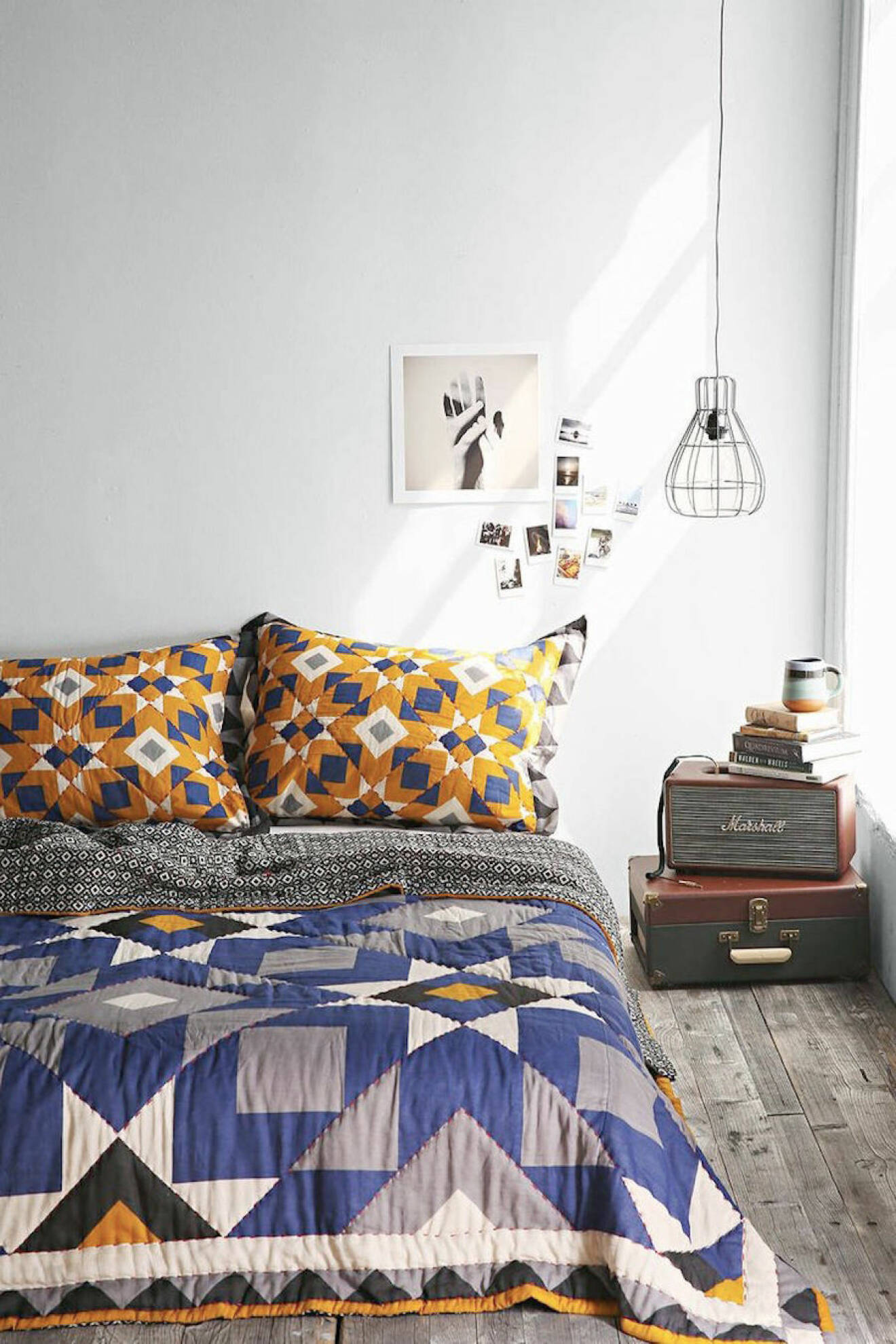Färgstark säng på golvet och ett sängbord av en gammal koffert och en högtalare