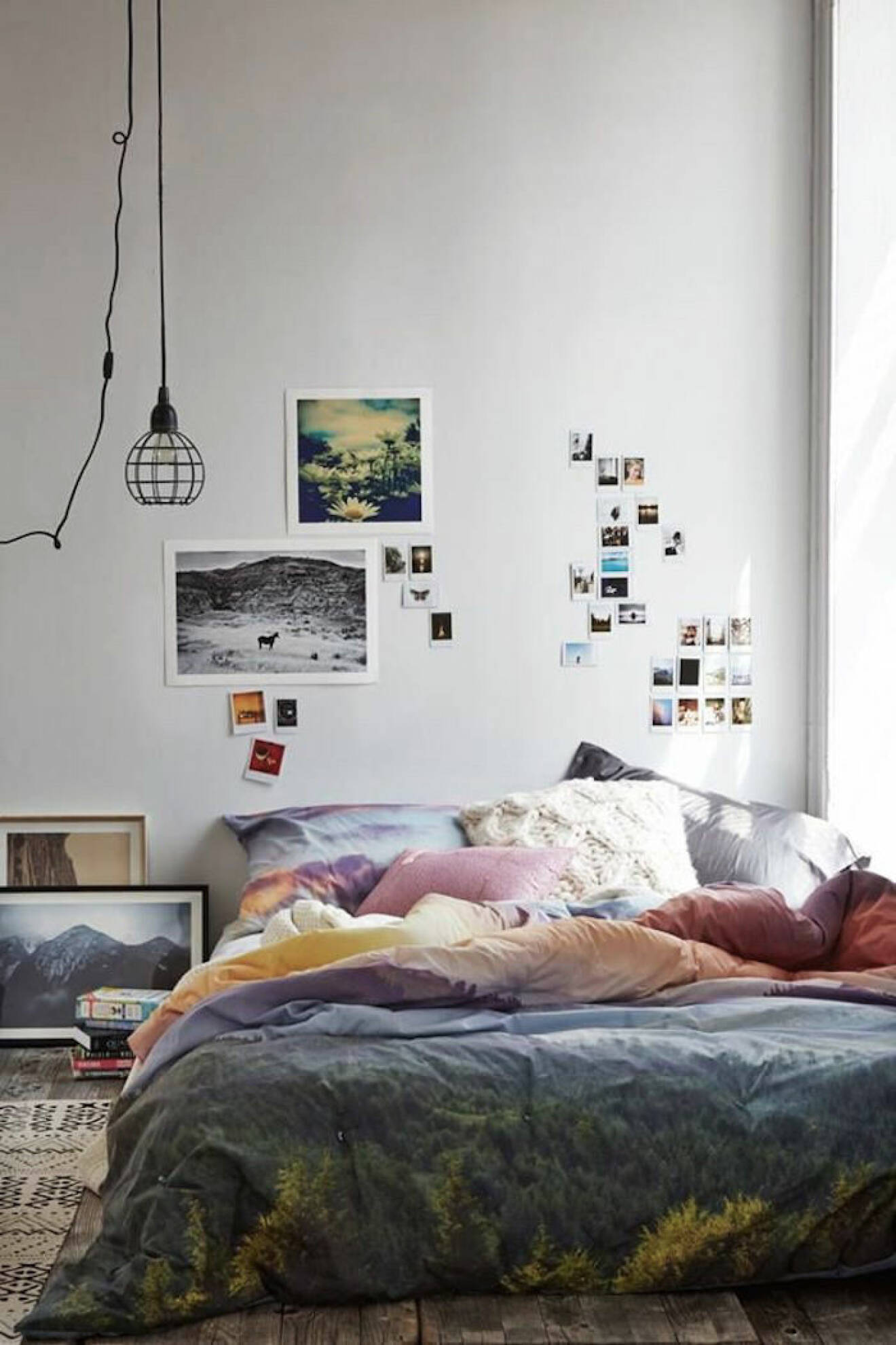 Säng på golvet och färgglada lakan. Foton på väggen.
