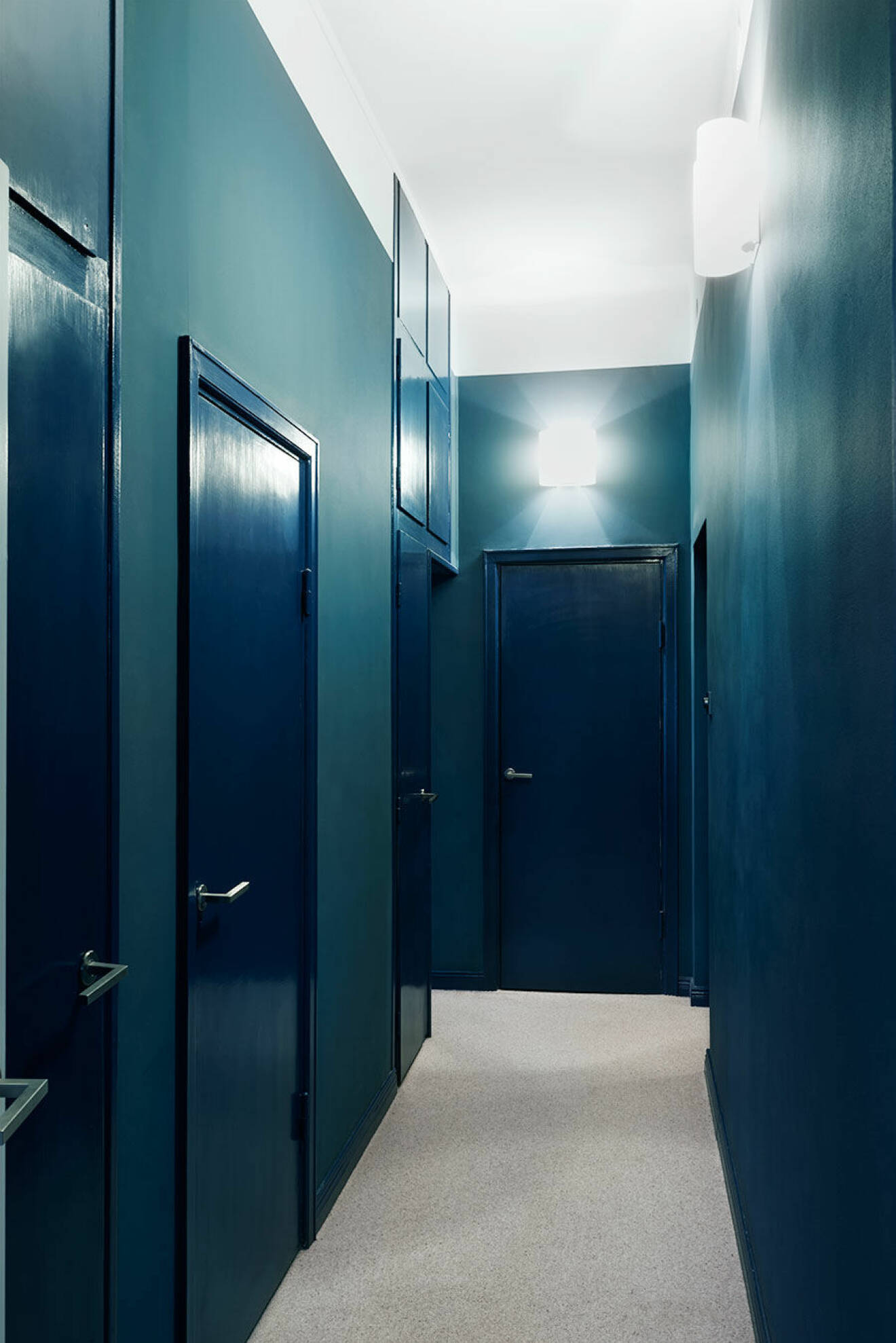 Korridoren med klädkammaren i ena änden och de tre sovrummen i fil längs med ytterväggen. Den avskilda privata känslan förstärks av den omboande heltäckningsmattan och färgvalen. Väggarna är målade i en helmatt blå nyans som står i effektfull kontrast mot dörrar och listers högblanka finish. ”Jag ville egentligen ha ännu mer färg”, säger Clara. 