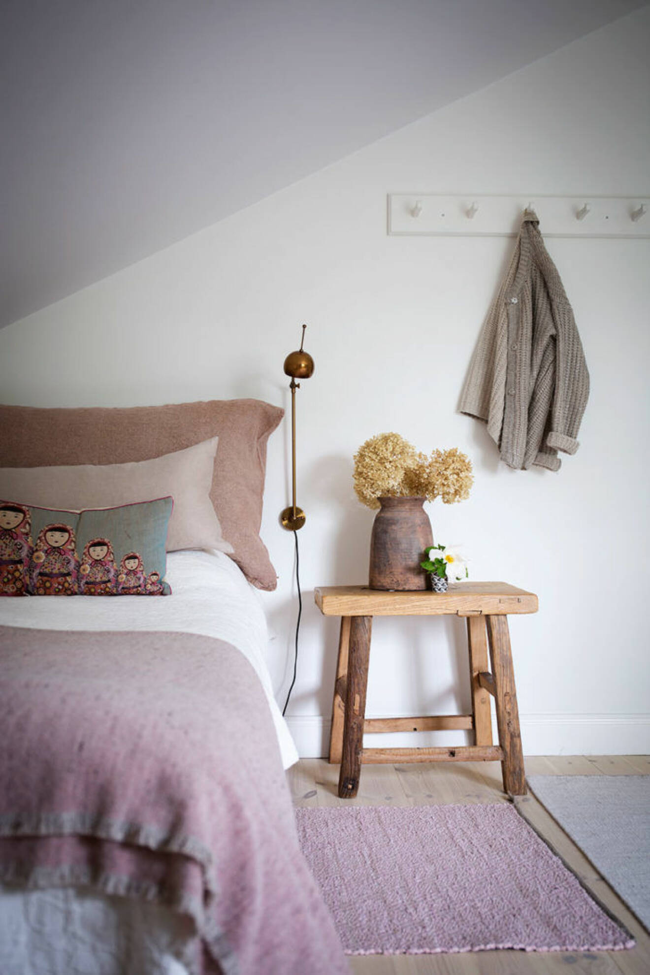 Sovrum med rosa toner och liten träpall som nattuksbord