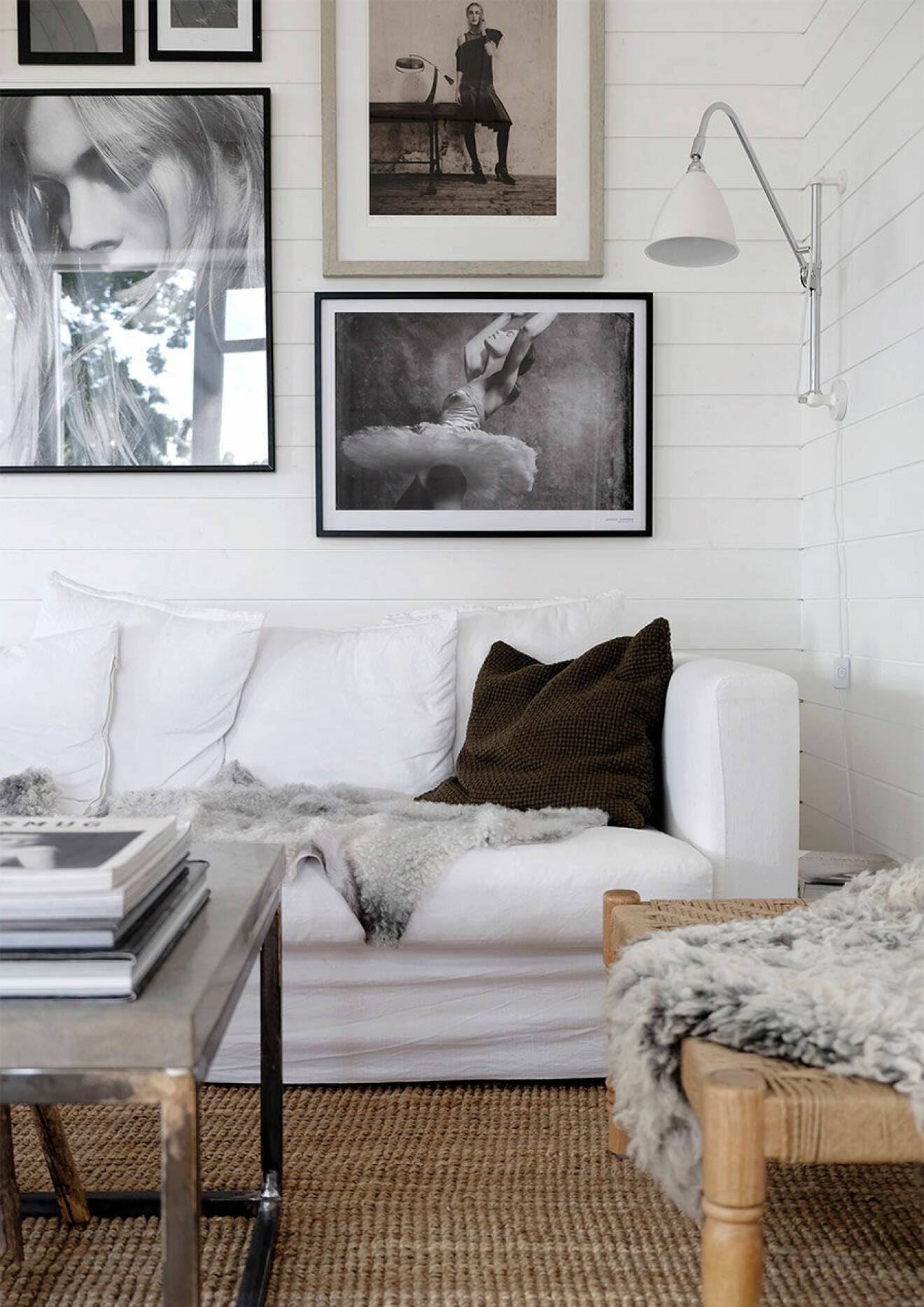 Stämningsfullt hörn av vardagsrummet med vit soffa, plädar och tavelvägg i bakgrunden