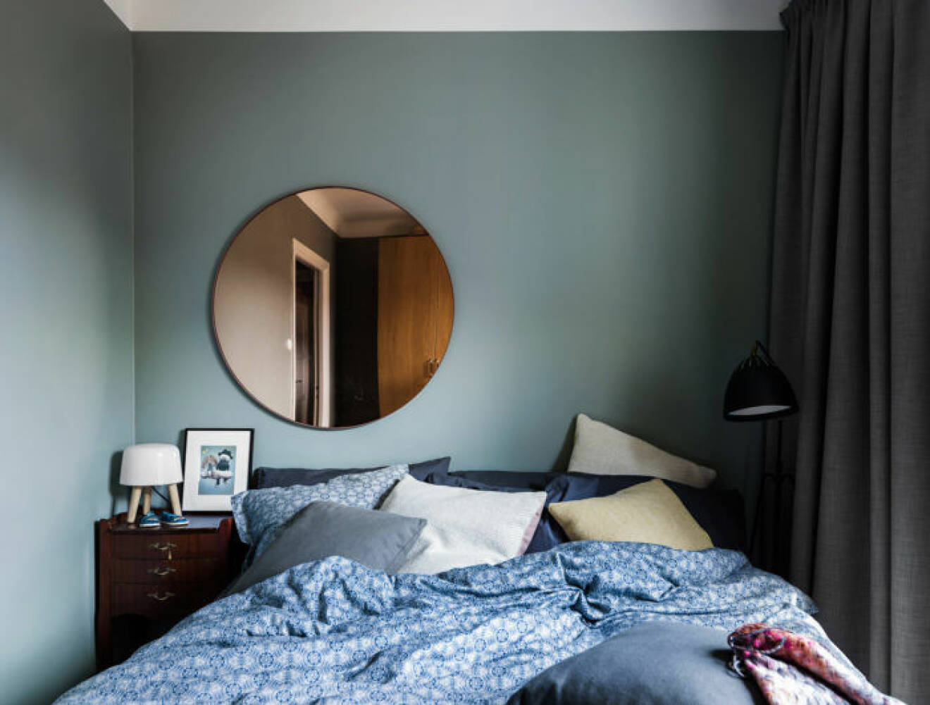 Sovrum med gröna väggar och en rund spegel i rosé