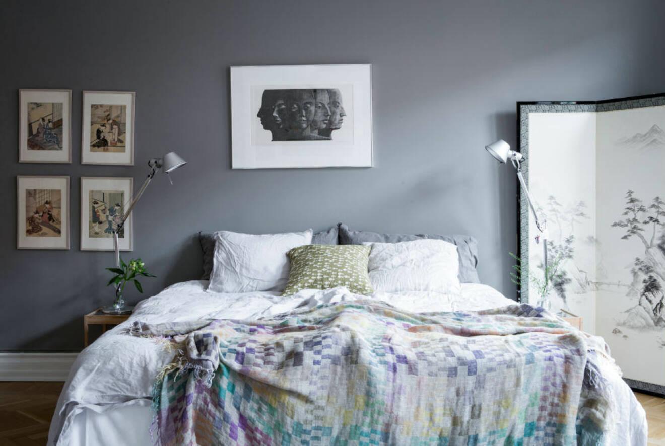 Sovrum med gråa väggar och en säng bäddad med skira multifärgade tyger och kuddar