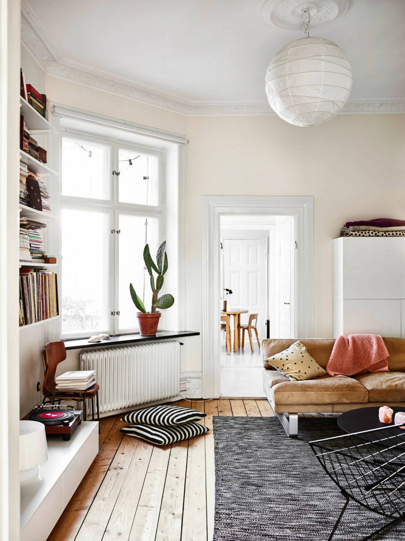 Vardagsrum med stora fönster, platsbyggd bokhylla och ljusa toner i hemmet i centrala Malmö